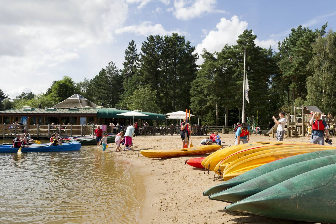 Families by the lake at Center Parcs Sherwood Forest, with kayaks pulled up on the beach